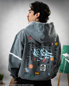 Person wearing a gray hoodie with various colorful patches on the back, against a neutral background.