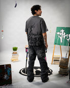 Person wearing a dark gray t-shirt with graphic designs in an indoor setting with art supplies and a plant.
