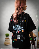 Person wearing a black t-shirt with colorful patches and designs, standing in a room.