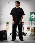 Person wearing a black t-shirt and pants in an indoor setting with books and plants.