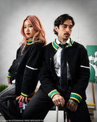 Man and women wearing a black knitted jacket with green and yellow accents in an indoor setting.