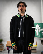 Man wearing a black knitted jacket with green and yellow accents in an indoor setting.